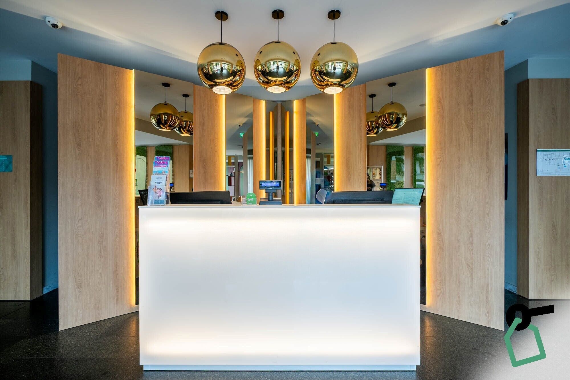 A reception desk with a white counter, surrounded by wooden panels and three golden spherical pendant lights.