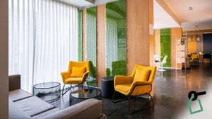 A modern lobby with two yellow chairs, a glass coffee table, and a black ottoman. - Hotiday Firenze Peretola (Florence)