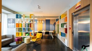 A modern hotel lobby with a central seating area, colorful bookshelves, and a visible elevator. - Hotiday Firenze Peretola (Florence)