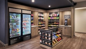 Un espace de caisses en libre-service comprenant un marché ouvert 24 heures sur 24, des distributeurs de boissons réfrigérées et des étagères remplies de collations et de boissons.
