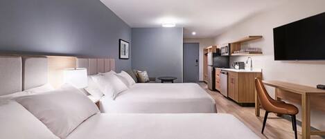 Ein Hotelzimmer mit zwei Betten, einem Schreibtisch, einem Stuhl, einem Fernseher und einer Küchenzeile.