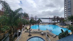 Een zwembad met een omliggend terras, palmbomen en uitzicht op water.