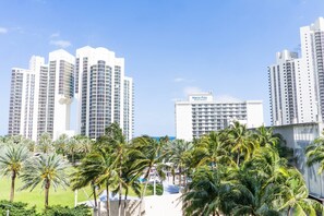 A high-rise hotel with a 'Marco Polo Beach Resort' sign, surrounded by palm trees and a clear sky. - Sunny Isles ocean-view 1BR: balcony, pool + gym, steps to beach (Sunny Isles Beach)