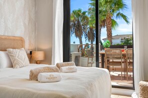 A hotel room with a large bed, a view of palm trees, and a balcony with wicker furniture. - Residence Velora Bay Estepona (Estepona)