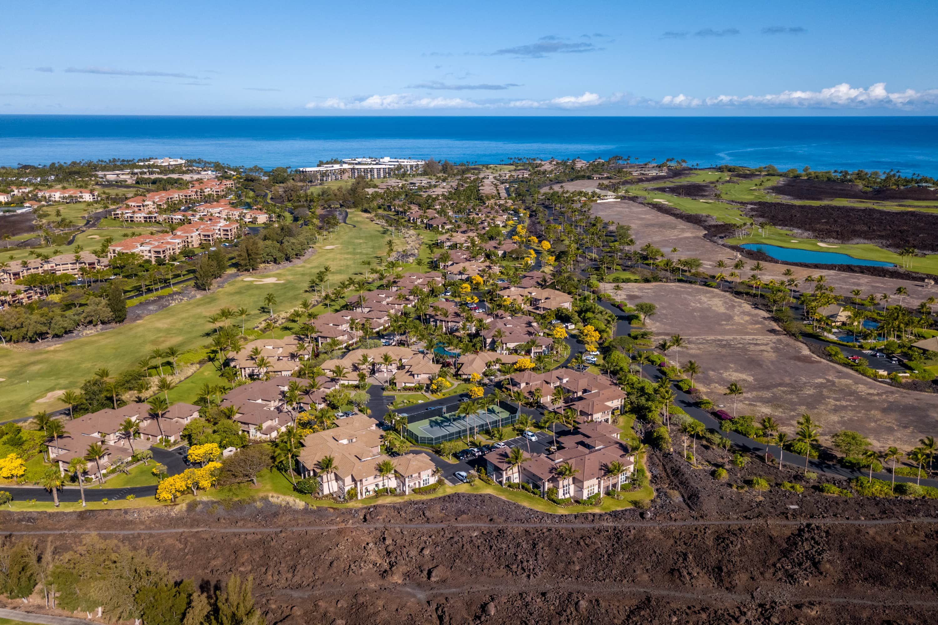 An aerial view of a coastal residential area with houses, a golf course, and a large hotel.