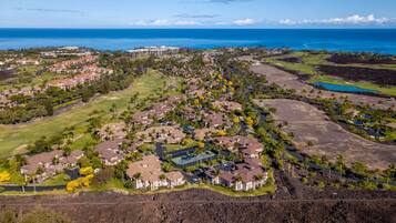 An aerial view of a coastal residential area with houses, a golf course, and a large hotel.