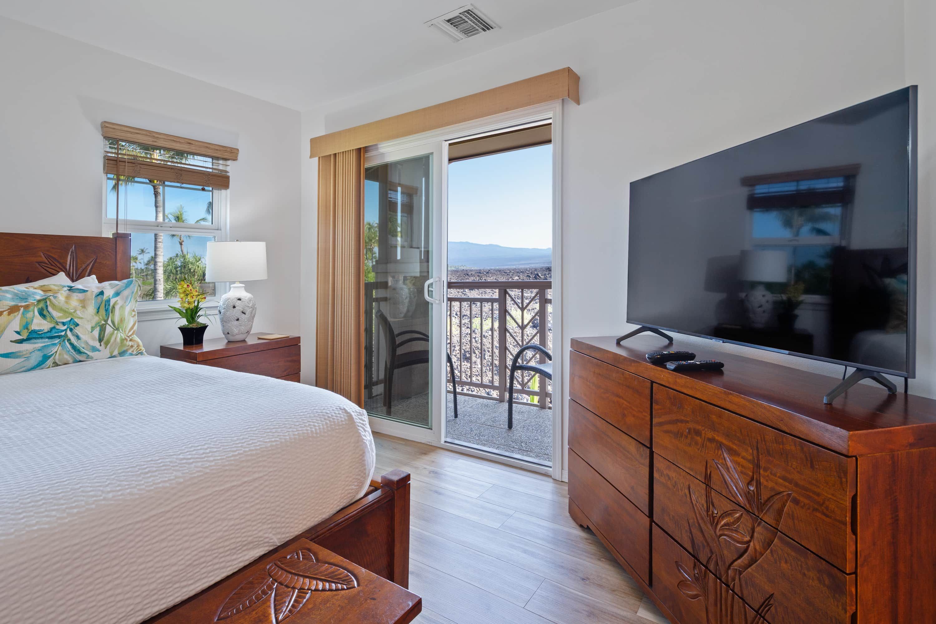 Un dormitorio con cama, televisión, cómoda y balcón con vistas.