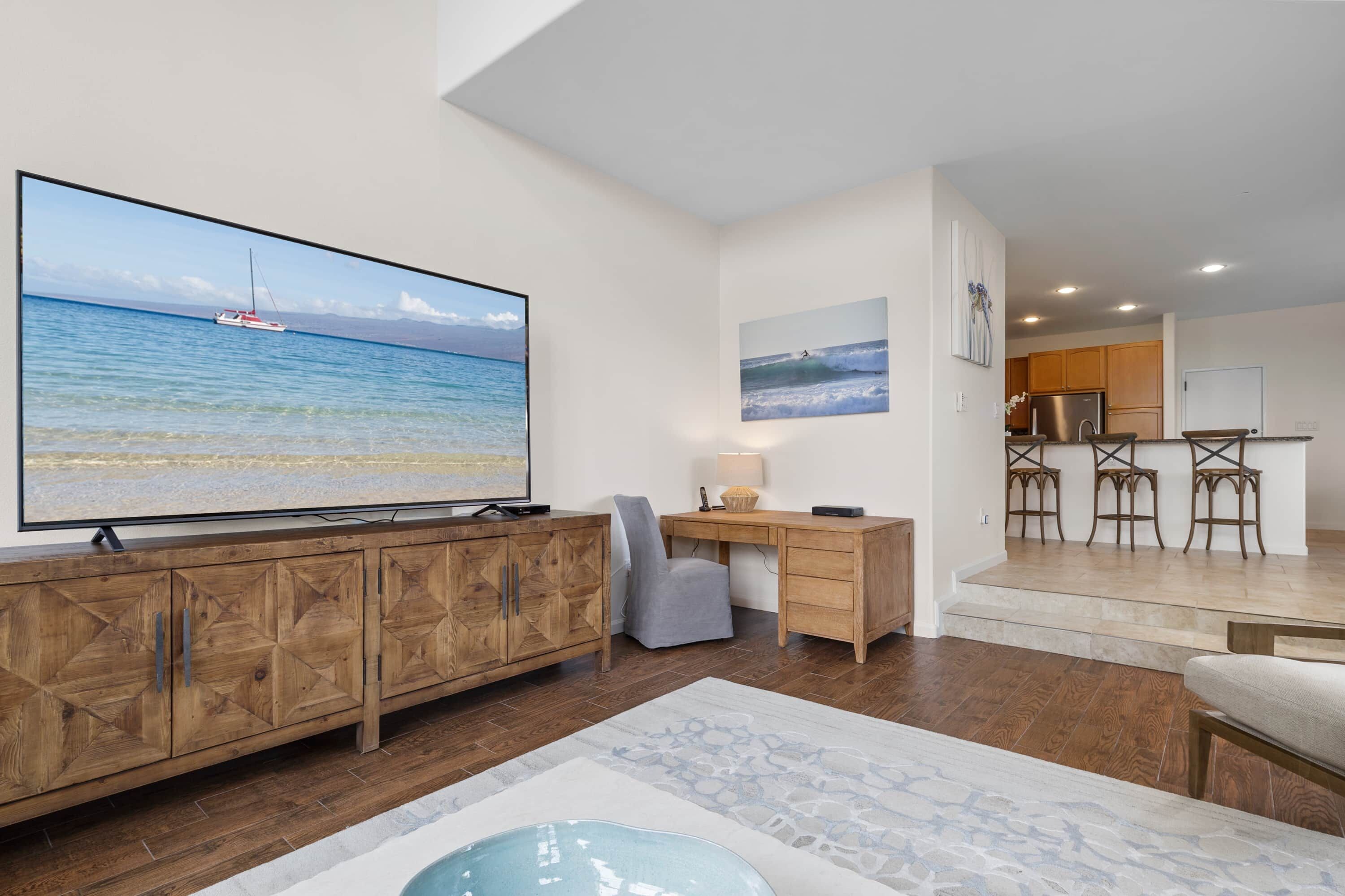 Un vaste espace de vie doté d’un grand téléviseur à écran plat diffusant des images de plage, de meubles en bois, d’un bureau et d’un coin salon confortable.