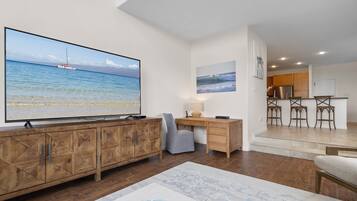Un vaste espace de vie doté d’un grand téléviseur à écran plat diffusant des images de plage, de meubles en bois, d’un bureau et d’un coin salon confortable.