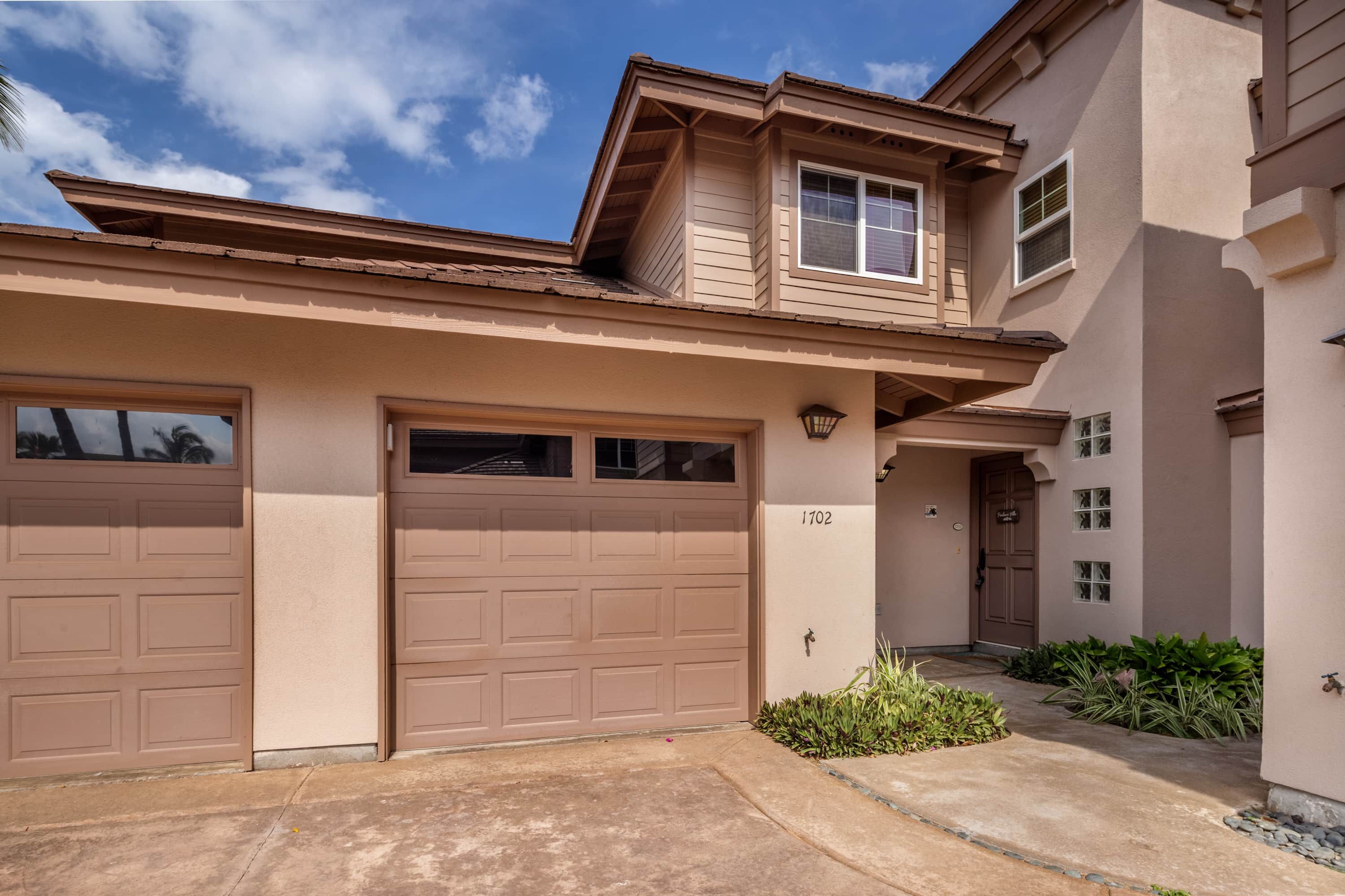 A two-story house with beige siding, a garage, and a small front yard with plants.
