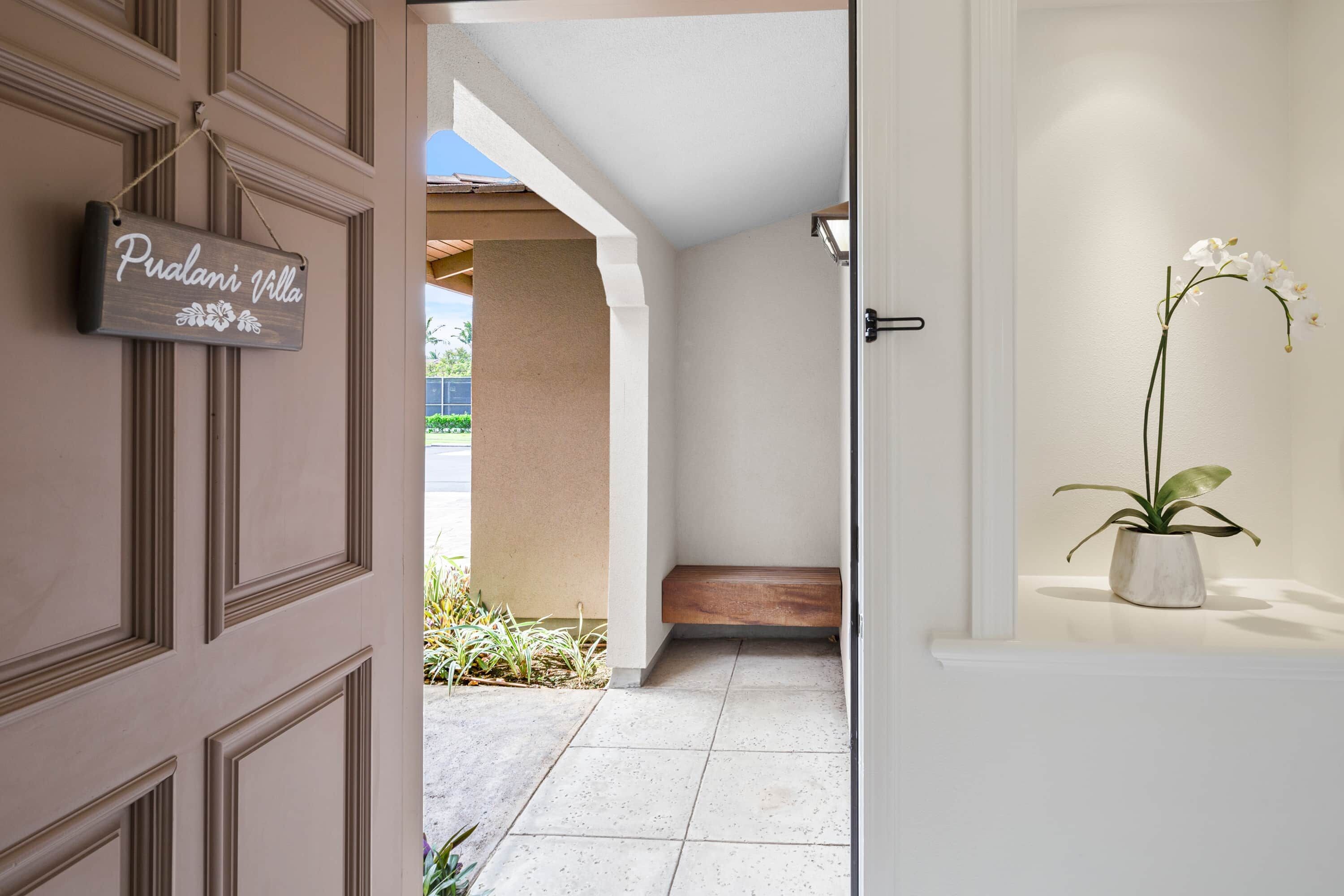 Un couloir avec une pancarte indiquant « Villa Pualani », une orchidée en pot posée sur une étagère et un banc dans le coin.