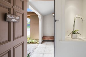 A hallway with a sign reading "Pualani Villa," a potted orchid on a shelf, and a bench in the corner. - Waikoloa Colony Villas 1702 (Waikoloa Village)