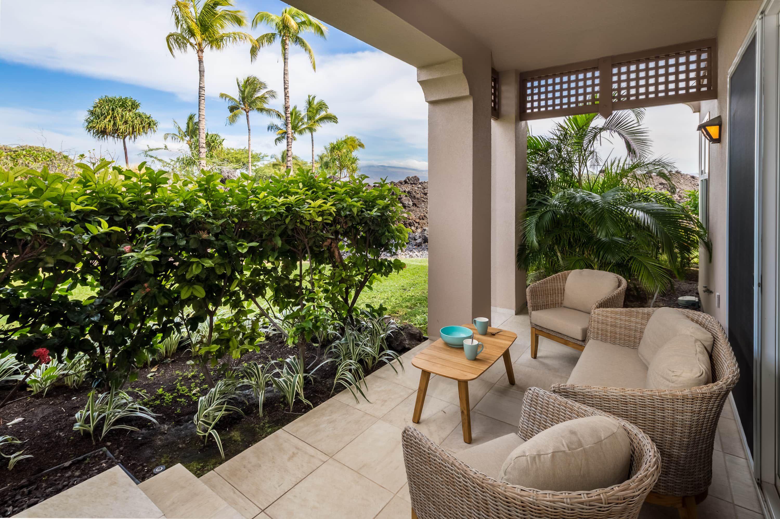 Un espace extérieur abrité, aménagé avec des meubles en osier, offrant une vue sur une végétation tropicale et un paysage rocheux.