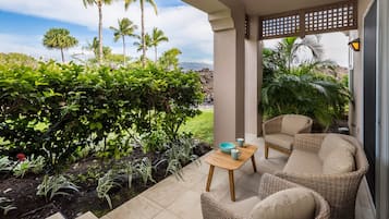 Un espace extérieur abrité, aménagé avec des meubles en osier, offrant une vue sur une végétation tropicale et un paysage rocheux.