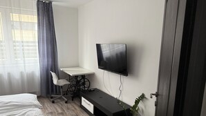 A modern hotel room with a bed, a desk with a chair, a flat-screen TV mounted on the wall, and a potted plant. - Modern family home near Debrecen Airport &City Center, with own bathroom&kitchen (Debrecen)