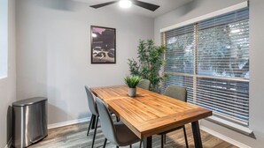 A dining area with a wooden table, chairs, a ceiling fan, a potted plant, a trash bin, and a window with blinds. - Arlington 1BR | AT&T, Globe Life, 6 Flags, Parking (Arlington)