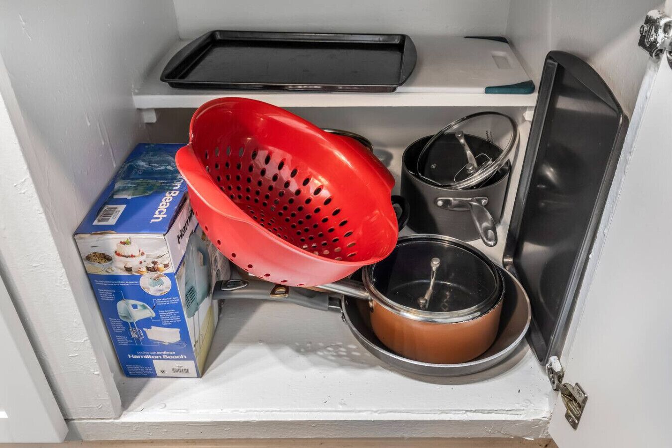 A kitchen with a red colander, a black tray, and a box of Hamilton Beach cookware.