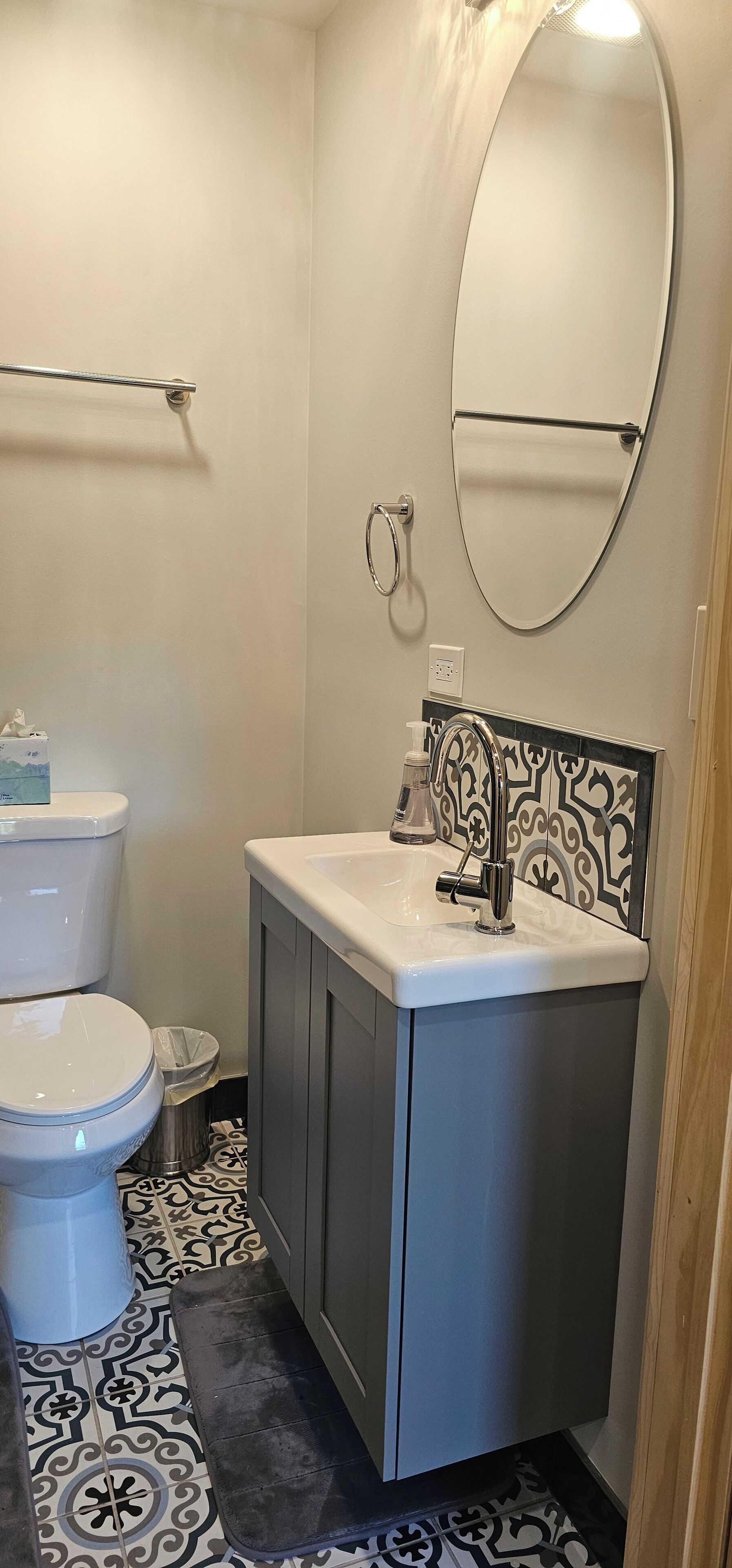 A bathroom with a toilet, sink, mirror, and patterned floor tiles.
