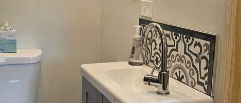 A bathroom with a toilet, sink, mirror, and patterned floor tiles.