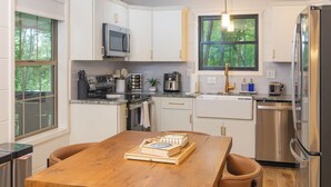 Une cuisine moderne avec des meubles blancs, des appareils en acier inoxydable et une table à manger en bois, assortie de chaises en cuir.
