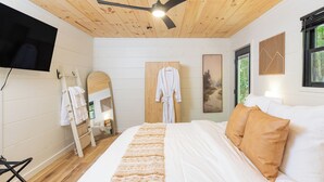 Une chambre à coucher comprenant un lit, un ventilateur de plafond, un téléviseur fixé au mur, une armoire en bois et une fenêtre donnant sur un paysage agréable.