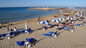 A beach with blue and white umbrellas, sun loungers, and a rocky breakwater in the background. - villa Kokalis resort 4 with private pool with a fantastic view (Γουβες)