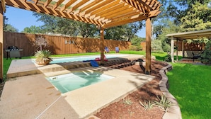 Un jardin avec une piscine, une pergola en bois et un espace patio couvert.