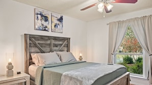 Une chambre à coucher avec une tête de lit en bois, un lit recouvert d’une couverture verte, une table de chevet avec une lampe et une fenêtre avec des rideaux.