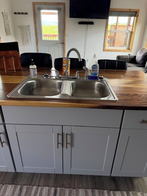 A kitchen with a stainless steel sink, wooden countertop, and white cabinets.