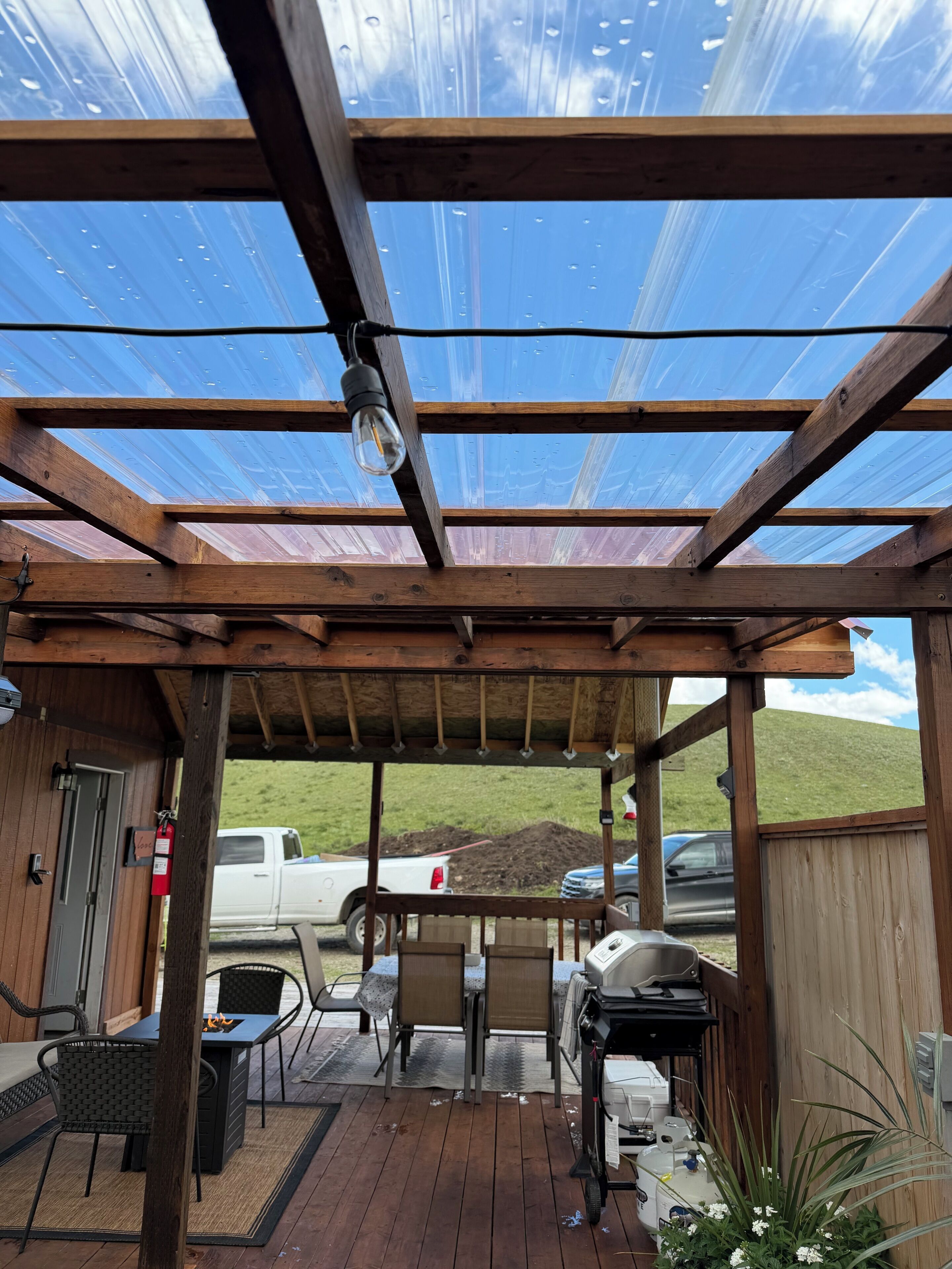 A covered outdoor area with a wooden deck, a grill, and a table with chairs.