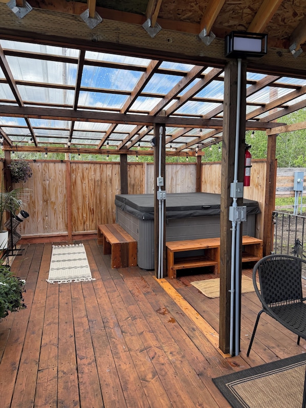 Une terrasse couverte avec un plancher en bois, un jacuzzi, des bancs et une chaise.