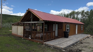 Une petite cabane en bois avec une véranda, une seule porte et une rampe menant à l’entrée.