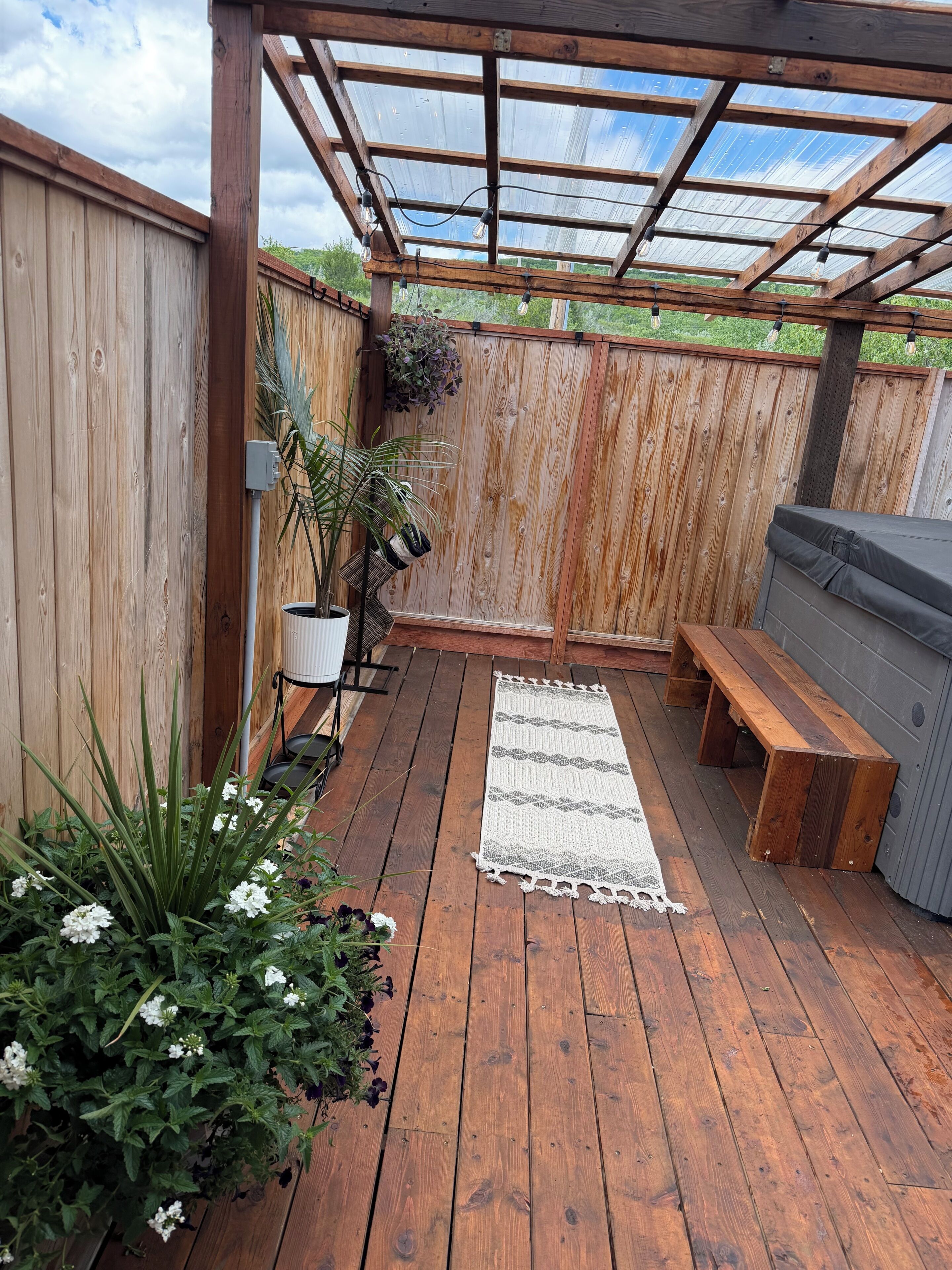 A wooden deck with a pergola, a bench, a grill, and potted plants.