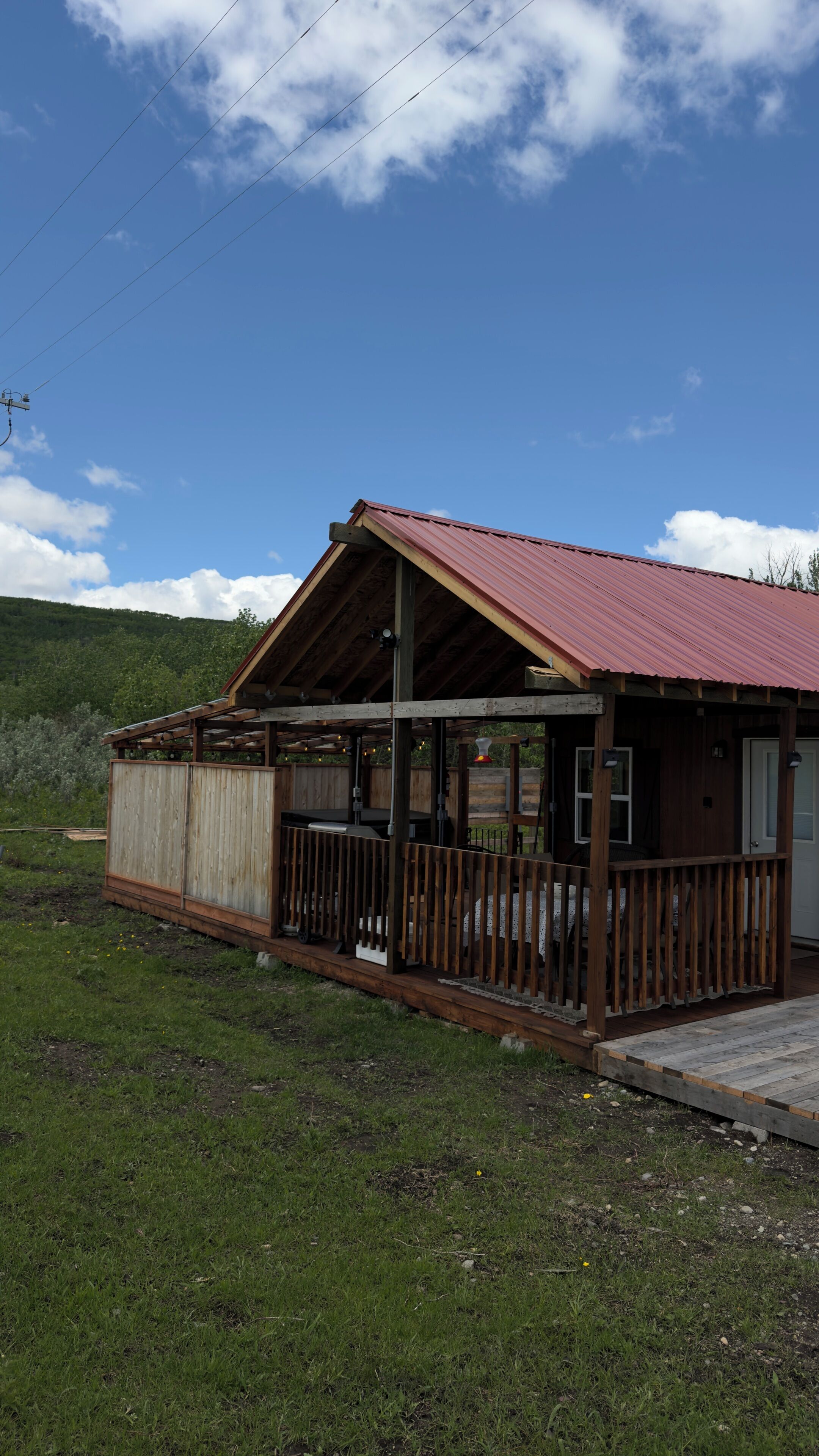 A rustic wooden building with a metal roof, a porch with wooden railings, and a grassy area in front.