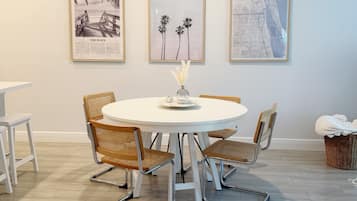 A dining area with a round table, four wicker chairs, and three framed artworks on the wall.