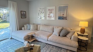 A living room with a large L-shaped sofa, a coffee table, and a lamp. There are three framed pictures on the wall. - NEW 3-bedroom house with AC in Vero Beach—13 min to beach! (Vero Beach)