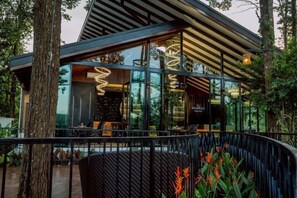A modern building with large glass windows, a wooden sloped roof, and outdoor seating. - High Tree Resort, Krabi (Krabi)