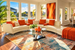 A modern living room with a sectional sofa, a glass coffee table, and a view of a residential area through large windows. - Luxury Lake Front +Private Dock +Kayak +Fishing +4BR, 3.5Bath +Sleeps 12 (Cypress)