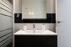 A bathroom with a white sink, two white bottles, and a mirror above the sink. - Spacious and luminous apartment in Plaza de España (Madrid)