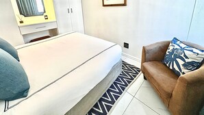 Un dormitorio con cama, armario, mesita de noche con lámpara, cuadro enmarcado en la pared y alfombra estampada.