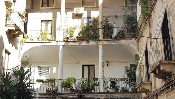 Un cortile con una motocicletta parcheggiata al centro, circondato da edifici con balconi e piante in vasi.