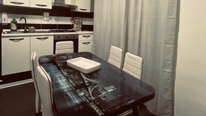 Una cucina compatta con mobili bianchi, un tavolo da pranzo nero e una sedia bianca.