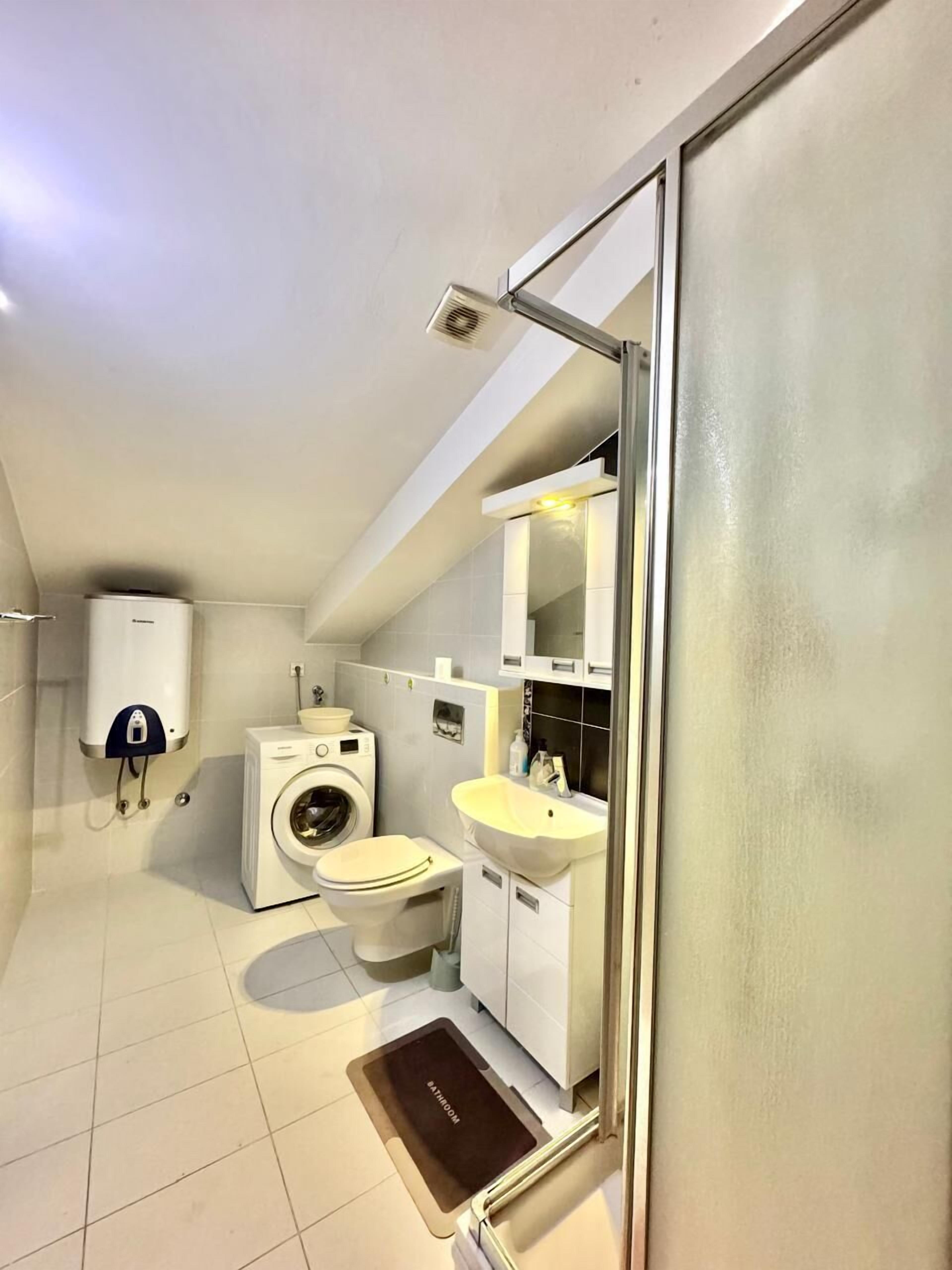 A compact bathroom with a washing machine, toilet, and sink.