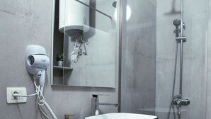 Uma casa de banho moderna com um espelho grande, um lavatório preto escultural, um secador de cabelo e um chuveiro.