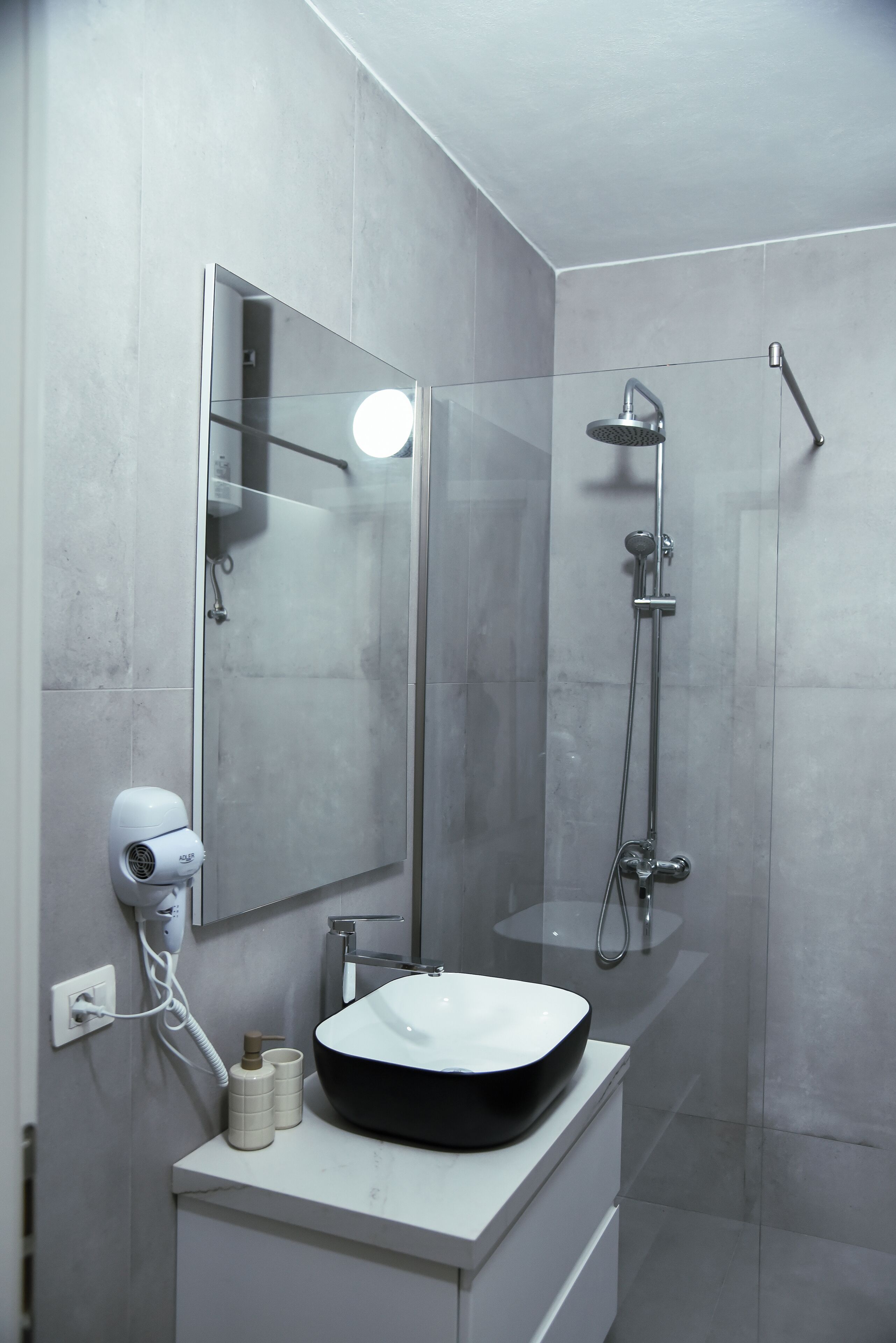 Een moderne badkamer met een grote spiegel, een witte wastafel en een douchecabine met glazen wanden.