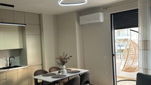Uma sala de estar moderna com um sofá, uma mesa de jantar com cadeiras, uma mesinha redonda com uma planta e uma cadeira suspensa perto da janela.