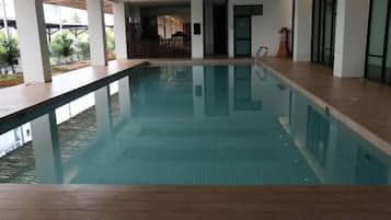 An indoor swimming pool with clear water, surrounded by a wooden deck and white walls.
