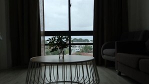 A modern living room with a round table, a sofa, and a large window with a view of buildings and trees. - Zen66 @ Roxy Serviced Apartment (Kuching)