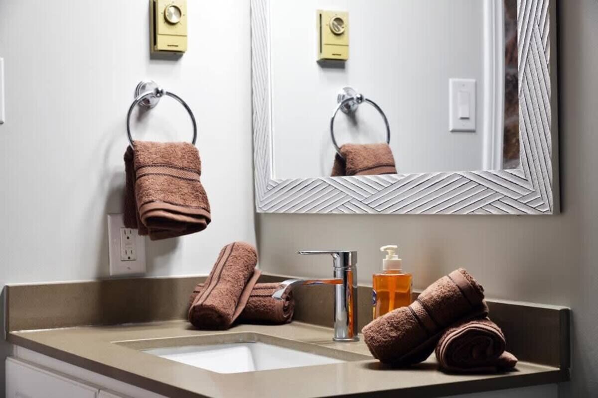 A bathroom with a sink, mirror, towel rack, and toiletries.
