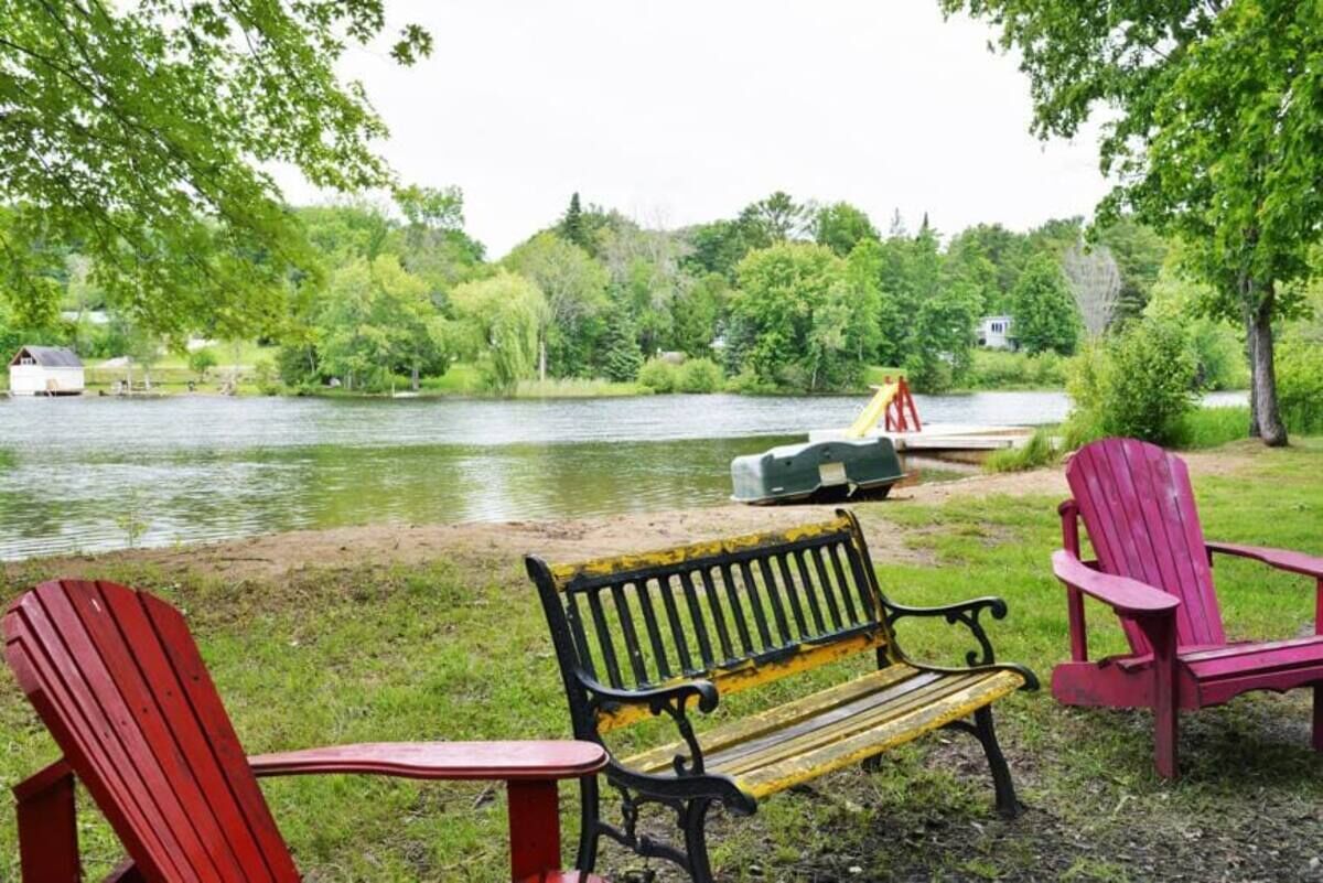 Un parc au bord du lac, avec un banc, des chaises Adirondack rouges et un canoë.